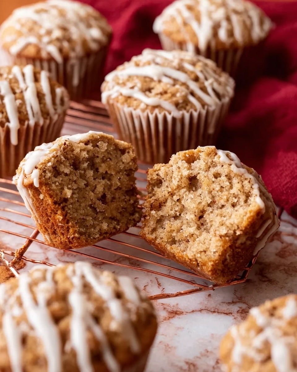 The image shows several muffins with light brown tops and a white icing drizzle on top. The muffins sit on a white paper liner that exposes the soft, crumbly texture inside. One muffin is split in half at the front, showing a fluffy, moist interior with little brown specks throughout. The muffins rest on a copper wire rack placed on a white marbled surface, with a red cloth underneath adding a warm background color. The overall look is cozy and inviting, highlighting the texture and icing detail on each muffin photo taken with an iphone --ar 4:5 --v 7