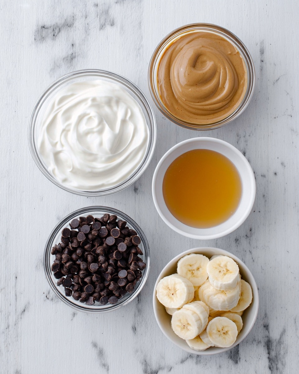 Peanut Butter Chocolate Frozen Greek Yogurt Bark Recipe 5 The image shows five clear glass bowls and one small white bowl arranged on a white marbled surface. The top left bowl contains thick, white yogurt with a smooth, creamy texture swirling gently. To its right, there is a bowl filled with smooth, light brown almond butter. Below the yogurt, there is a bowl filled with small, dark brown chocolate chips that have a shiny surface. Next to the chocolate chips is the white bowl containing a light golden honey-like syrup with a glossy surface. To the right of that, there is a bowl with evenly sliced rounds of pale yellow bananas, each showing a soft texture and slight brown specks in the center. photo taken with an iphone --ar 4:5 --v 7
