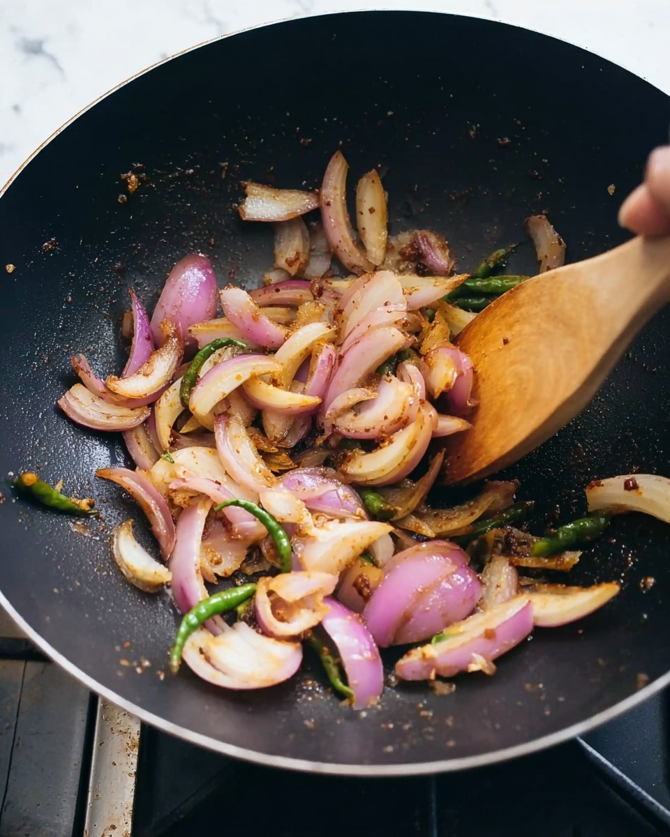 A close-up of a black wok on a stove with sliced red onions and green chili pieces being cooked. The onions are soft and lightly browned, with some pieces turning golden yellow. A wooden spoon is stirring the mixture, its shape slightly blurred by motion. The cook uses a woman's hand to hold the spoon, visible at the top right corner of the image. The wok surface inside shows some oil and spices, adding a slight shine and texture. The background is a white marbled texture. photo taken with an iphone --ar 4:5 --v 7