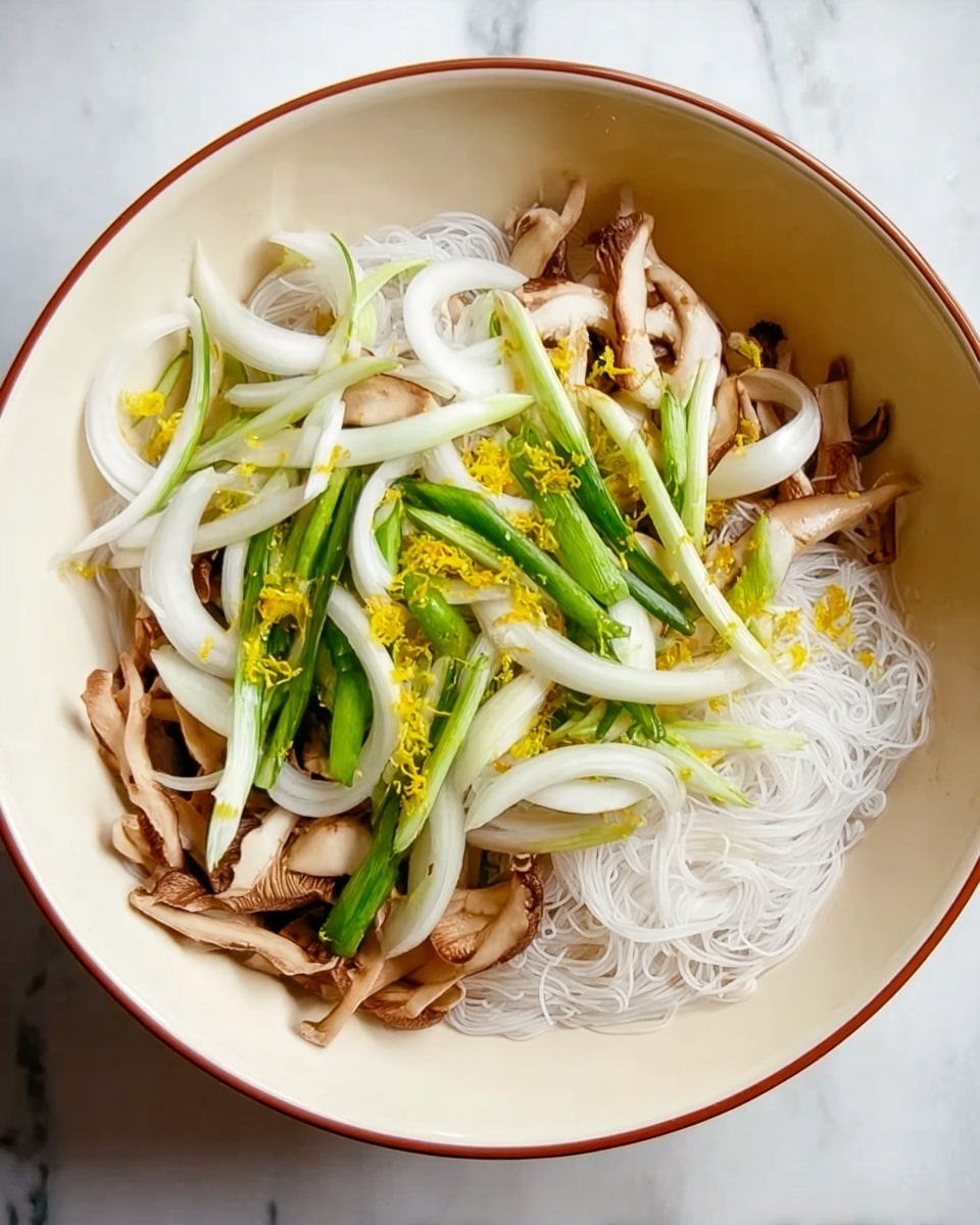 A white bowl contains three main layers: at the bottom are thin, translucent white rice noodles with a slight texture; above them are brown mushroom slices with smooth edges; and on top are many curved white onion slices mixed with long pale green onion pieces. Small bits of bright yellow zest are scattered over the top. The bowl sits on a white marbled surface. photo taken with an iphone --ar 4:5 --v 7