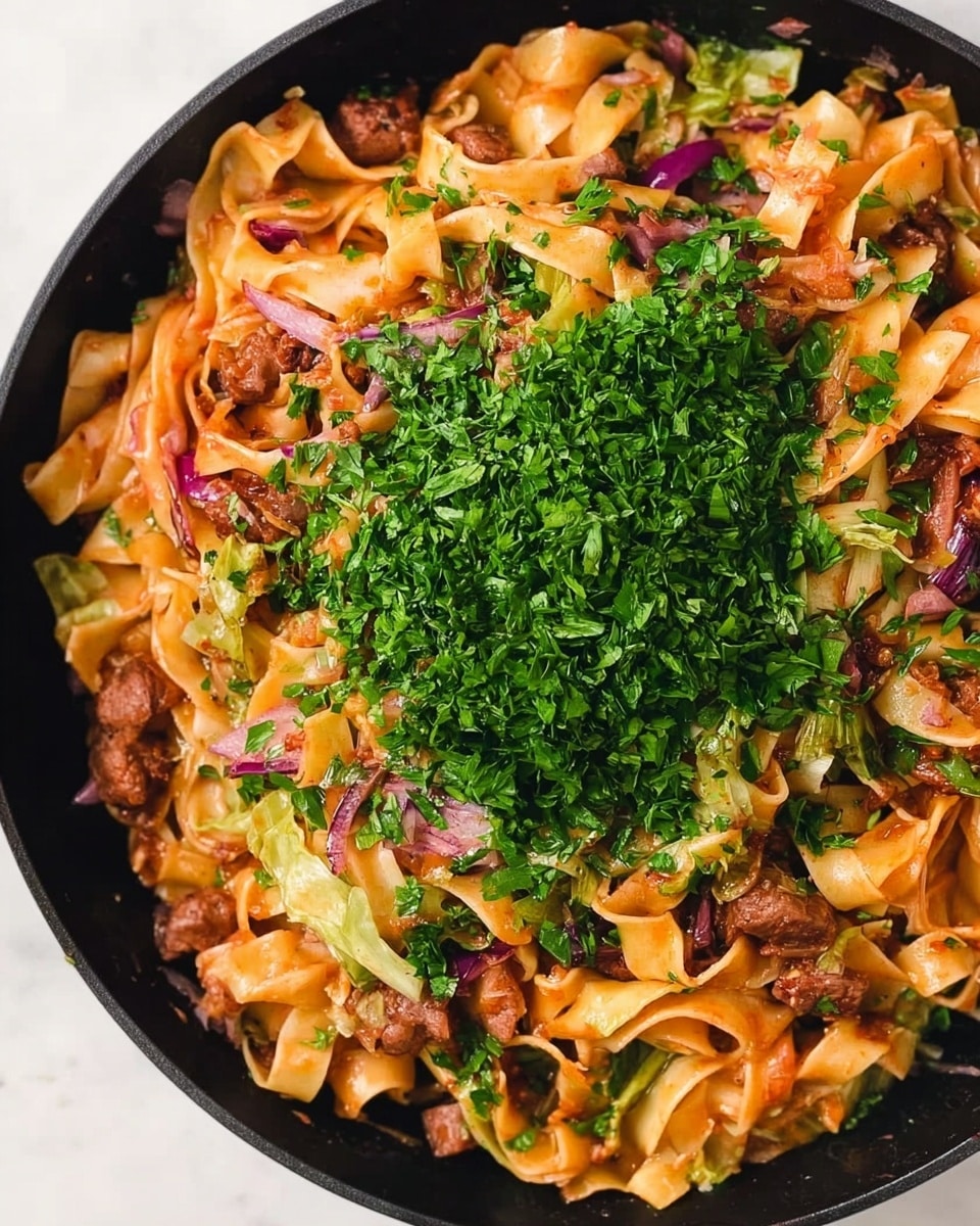 A close-up view of a black skillet filled with cooked wide noodles that are light orange from sauce, mixed with browned pieces of meat, red onion slices, and pale green cabbage. The top center of the dish is covered with a large pile of finely chopped fresh green herbs. The skillet sits on a white marbled surface. Photo taken with an iphone --ar 4:5 --v 7