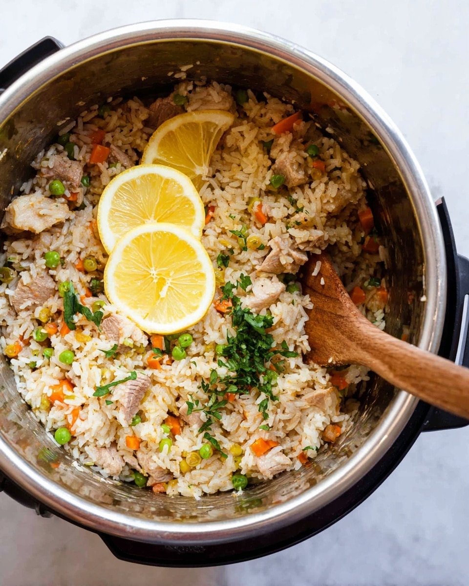 A close-up top view of a silver cooking pot filled with cooked rice mixed with small pieces of light brown meat, orange carrot bits, and green peas, creating a colorful textured layer. There are three thin slices of yellow lemon placed on top, along with fresh green herb leaves scattered around. A wooden spoon with a light brown handle is partially submerged on the right side of the rice mixture. The pot is set on a surface with a white marbled texture. photo taken with an iphone --ar 4:5 --v 7