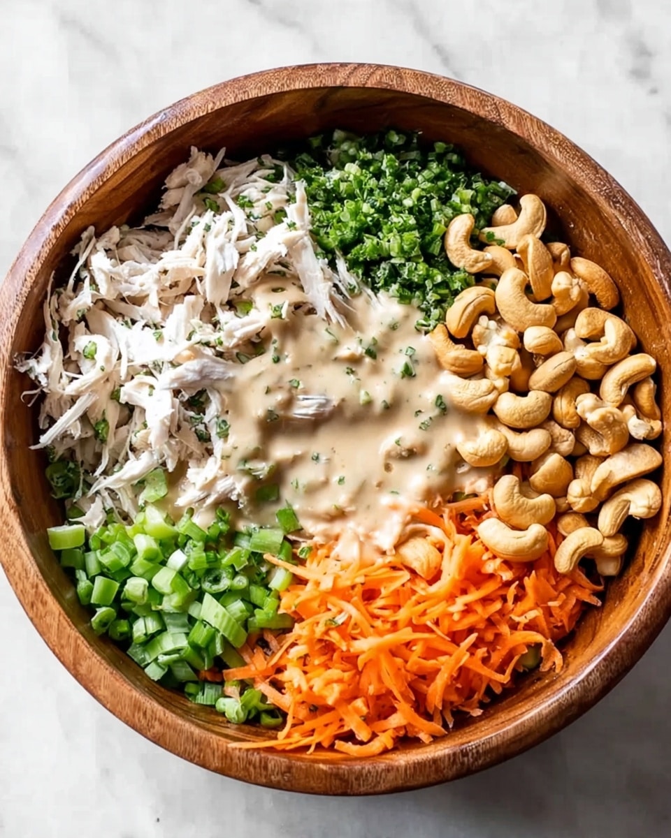 The image shows a wooden bowl with five different layers arranged side by side inside it. Starting from the top left, there is shredded white chicken, next to it is a pile of chopped green herbs, followed by a large group of whole cashew nuts on the top right. Below them, on the bottom right, are sliced green onions and on the bottom left are shredded orange carrots. A creamy light beige sauce is poured over the shredded chicken, cashews, carrots, and green onions. The bowl is placed on a white marbled surface. Photo taken with an iphone --ar 4:5 --v 7