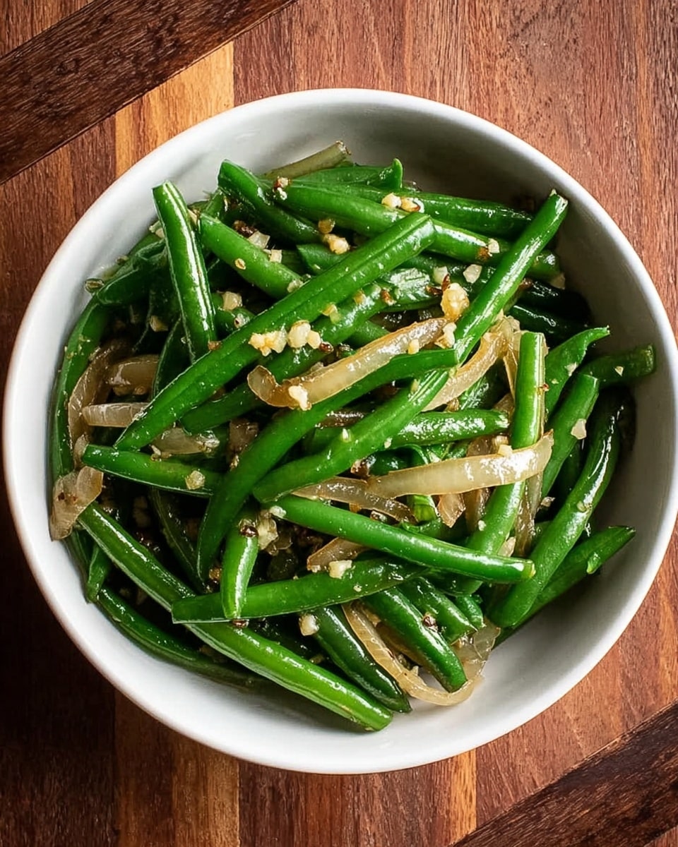 A white bowl filled with cooked green beans and slices of sautéed onion. The green beans are bright green, long, and whole, mixed evenly with translucent, slightly browned onion strips. Small bits of minced garlic are scattered on top, adding texture and a light beige color contrast. The bowl sits on a brown wooden surface, showing a rustic and warm setting. photo taken with an iphone --ar 4:5 --v 7