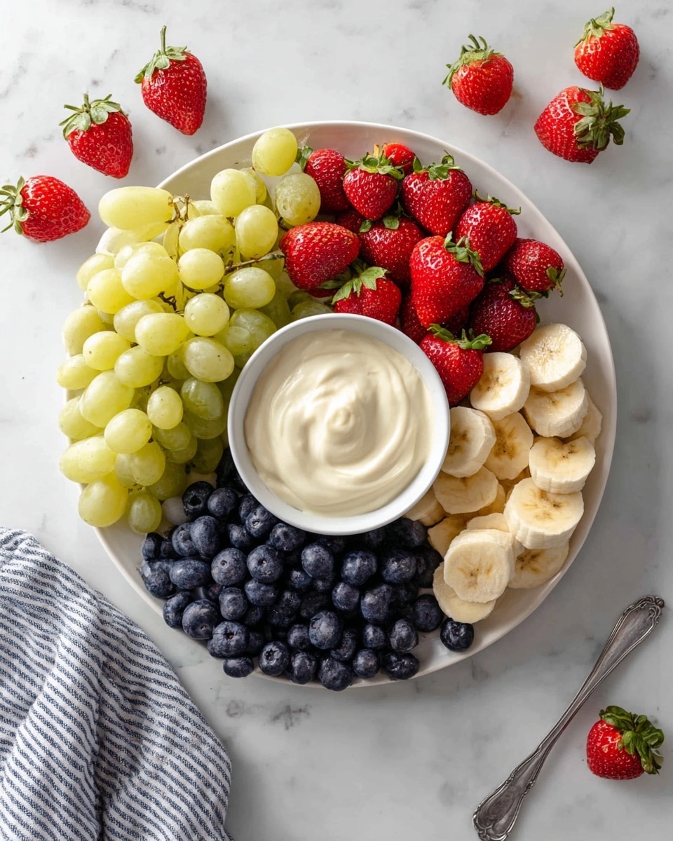A white plate sits on a white marbled surface, filled with fresh fruit arranged in four sections around a central small white bowl of creamy dip. Starting from the bottom left and moving clockwise, there is a bunch of light green grapes with a smooth, shiny texture, followed by bright red strawberries with green leafy tops, then a pile of dark blue, round blueberries, and finally several slices of pale yellow banana with a smooth surface. Around the plate, a few strawberries and grapes are scattered, and a striped cloth and a spoon are placed nearby. photo taken with an iphone --ar 4:5 --v 7