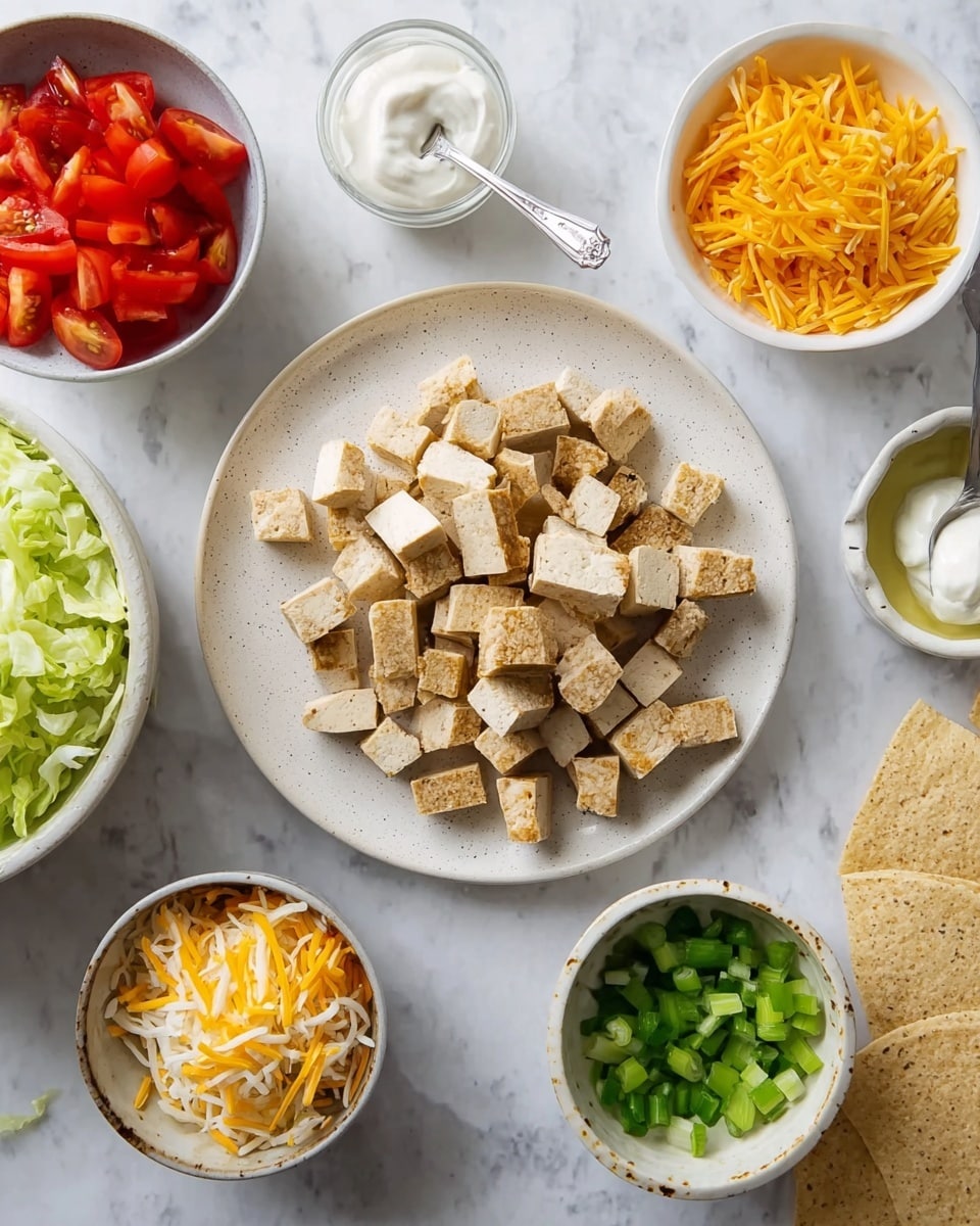 The image shows a white round plate in the center with many pieces of cooked light brown tofu, cut into short strips and small squares. Around the main plate, there are five small white bowls placed on a white marbled surface. The top left bowl contains small red tomato halves, the bottom left bowl is filled with light green shredded lettuce, the bottom center bowl holds a mix of shredded yellow and white cheese, the top right bowl has a dollop of white sour cream with a small silver spoon, and the bottom right bowl contains chopped bright green scallions. Near the bottom right corner, there are two rectangular beige crackers with visible holes. A woman's hand is not visible in this image. Photo taken with an iphone --ar 4:5 --v 7