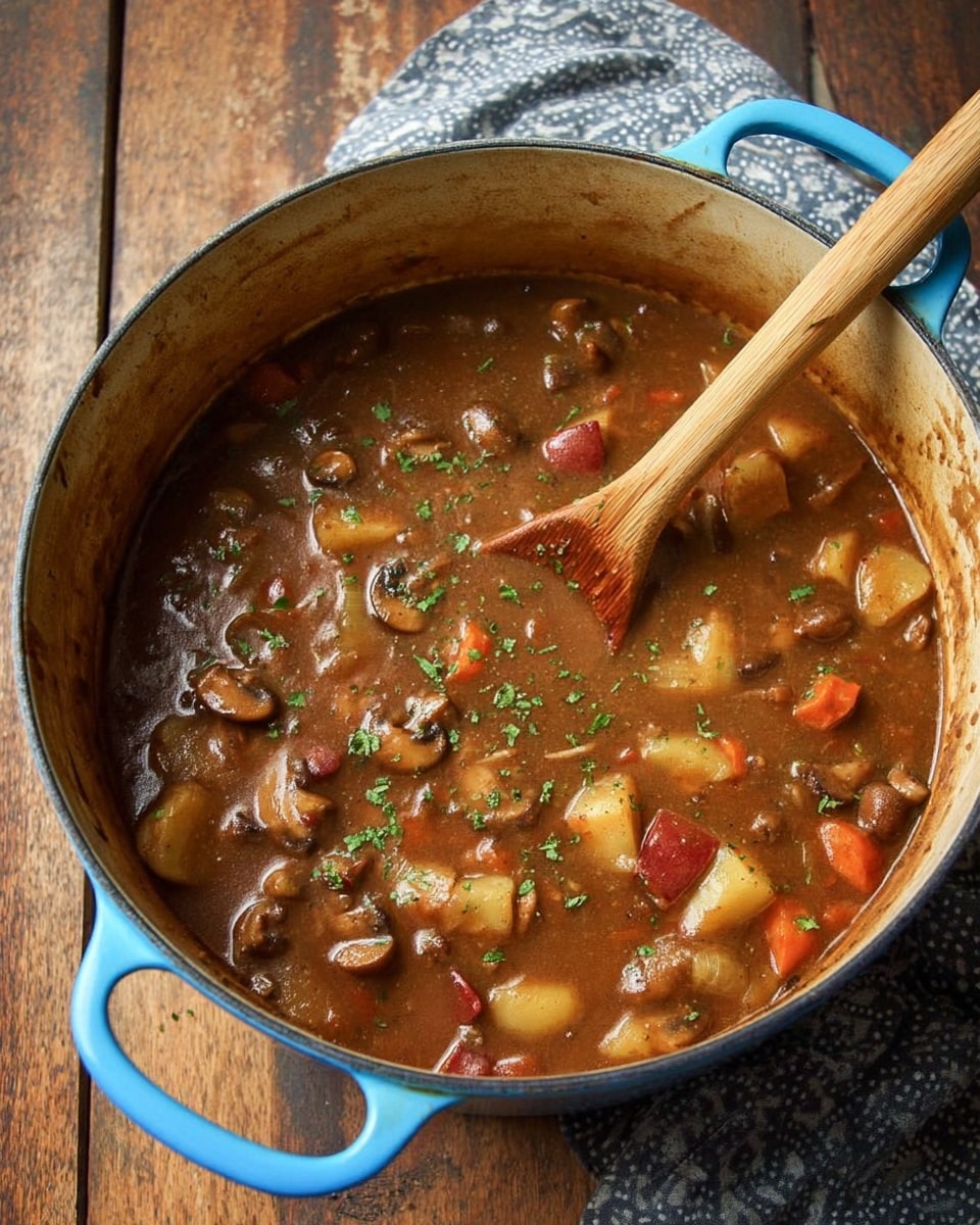A blue cooking pot filled with thick brown stew that has chunky pieces of red-skinned potatoes, mushrooms, carrots, and celery. The stew is covered with small green herb sprinkles and has a wooden spoon resting inside, its handle leaning against the pot's edge. The pot sits on a wooden surface next to a grey patterned cloth. photo taken with an iphone --ar 4:5 --v 7