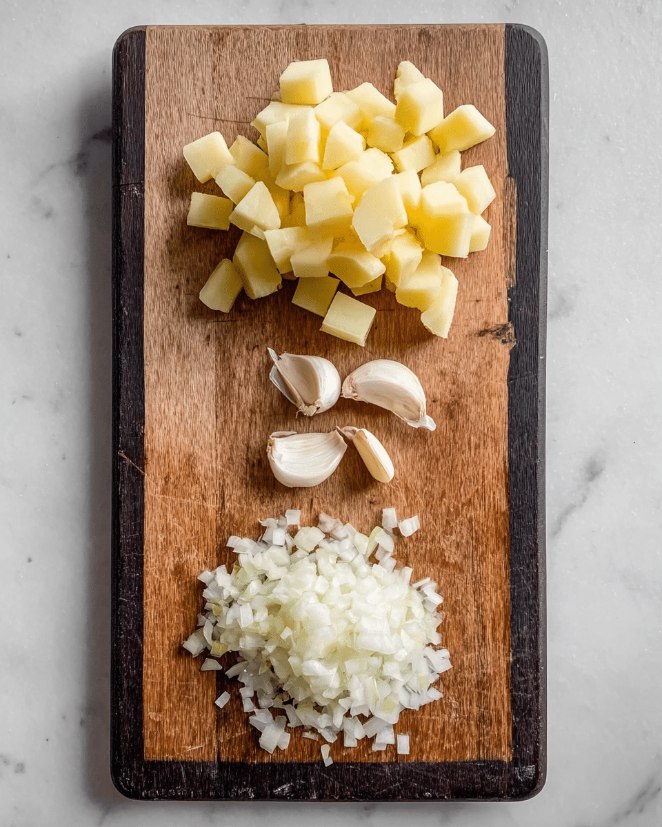 A wooden cutting board with a black top edge is placed on a white marbled surface. On the board, there are three piles of ingredients arranged vertically: at the top right, a pile of light yellow potato cubes with smooth surfaces; in the middle left, a small group of peeled garlic cloves, white with smooth texture; and at the bottom, a heap of finely chopped white onions, slightly translucent with small square pieces. The light from above casts soft shadows around the ingredients. photo taken with an iphone --ar 4:5 --v 7