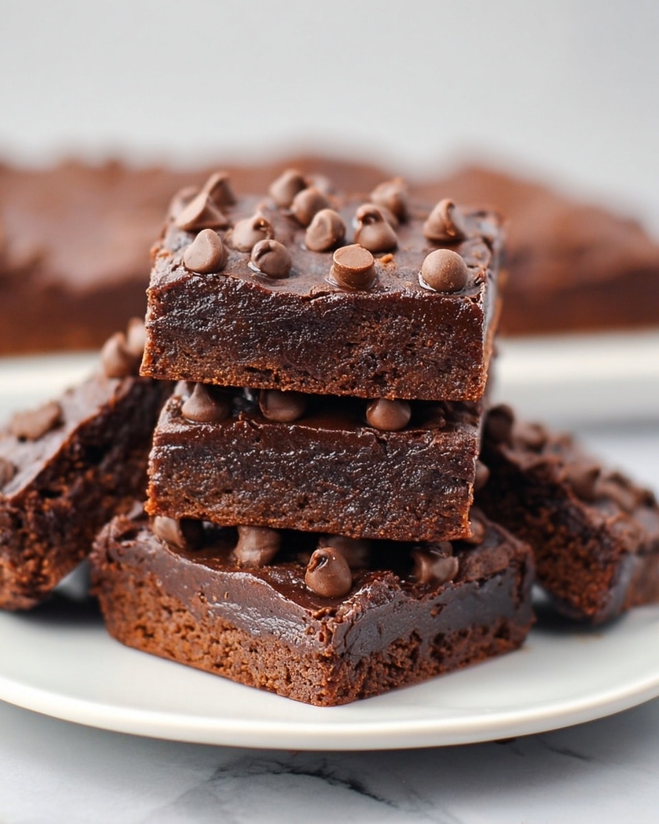 A stack of five square chocolate brownies sits on a white plate, placed on a white marbled surface. Each brownie has two visible layers: a dense, dark brown base and a slightly shiny, darker chocolate layer on top. The top layer is generously covered with medium-sized milk chocolate chips, giving the surface a bumpy texture. The brownies are arranged with one in front showing its full top and side, and the others stacked and leaning behind it, creating a sense of depth. photo taken with an iphone --ar 4:5 --v 7