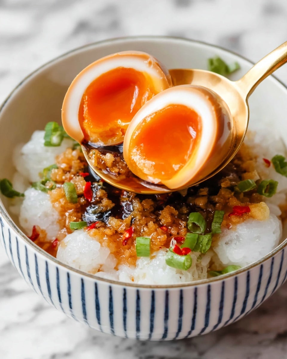 A close-up of a bowl with three layers: the bottom layer is white sticky rice with a soft texture, topped with small pieces of green onion and red chili. Above the rice is a layer of dark soy sauce mixed with tiny bits of brown fried garlic and other seasonings. The top layer consists of two halves of a shiny brown marinated egg with a soft, bright orange yolk inside, held by a golden spoon above the bowl. The bowl is white with blue vertical stripes on the inside, and it sits on a white marbled surface. photo taken with an iphone --ar 4:5 --v 7