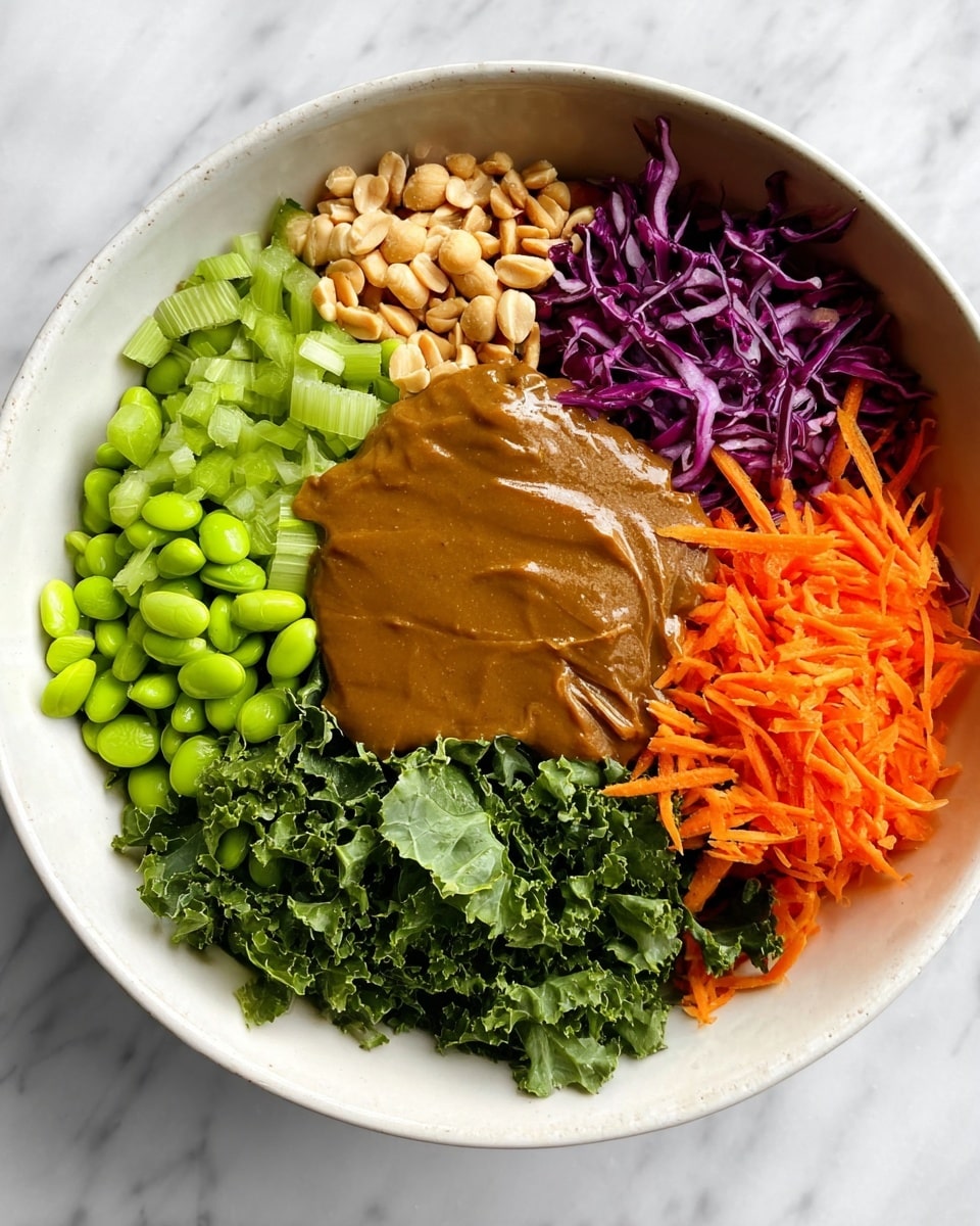 A white bowl holds a colorful mix of fresh ingredients arranged in layered sections against a white marbled surface. Starting at the bottom left, bright green edamame beans form one thick layer. Above them, light brown peanuts are piled next to dark green, curly kale leaves. Shiny chopped leafy greens sit next to the kale. To the right of the greens, thin slices of light green celery are visible before deep purple chopped cabbage makes a vibrant layer at the top-right. Bright orange shredded carrots fill the bottom right side of the bowl. In the middle, a smooth, thick brown sauce spreads over the carrots and celery. The photo was taken with an iphone --ar 4:5 --v 7
