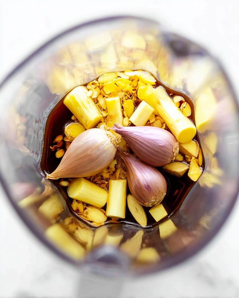 Inside a clear blender jar, there are about three layers of ingredients visible. The bottom layer is a dark brown liquid, smooth and shiny. On top of this, there are thick small pieces of pale yellow root, mixed with longer light yellow stalks cut into small parts. Resting on these, two medium-sized light purple shallots with smooth skin lie close to each other. The blender jar stands on a clean white marbled surface. Photo taken with an iphone --ar 4:5 --v 7