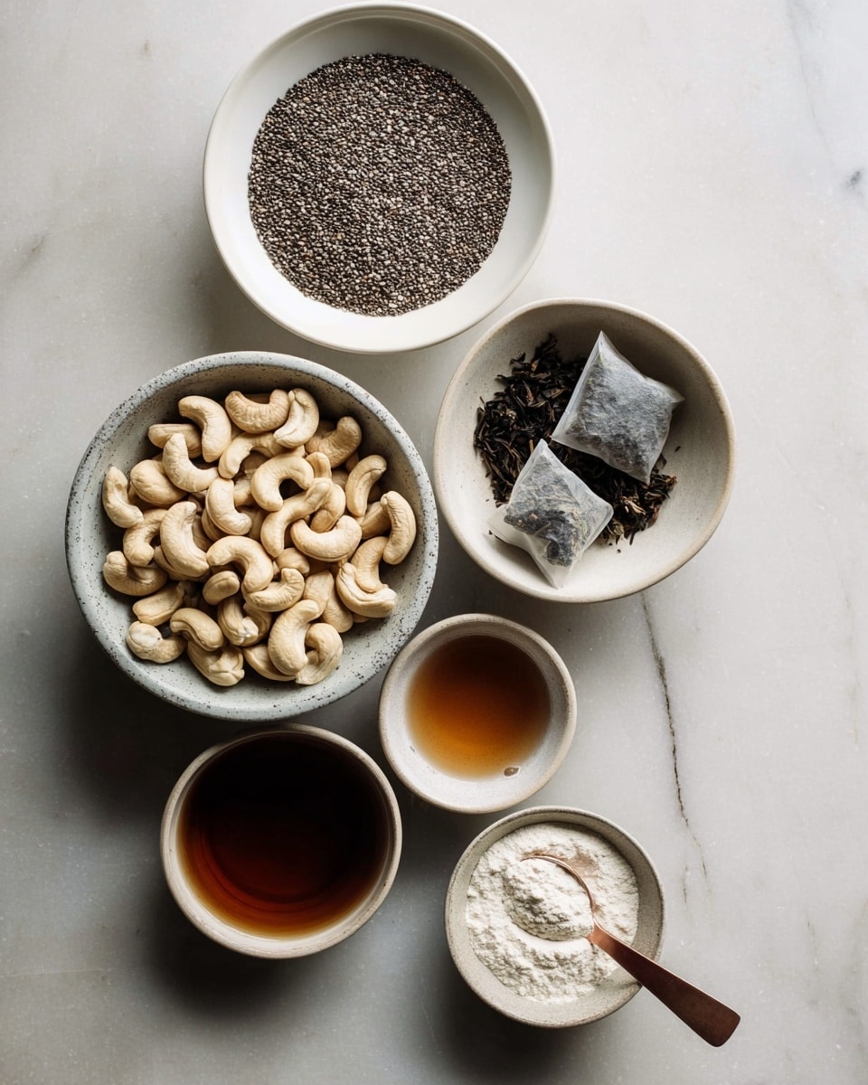 The image shows six white bowls arranged on a white marbled surface. The largest bowl at the bottom left holds many light beige cashew nuts with smooth curved shapes. Above it to the right, a medium white bowl contains dark tea bags on top of loose tea leaves, both with a rough texture. At the top center, a large white bowl is filled with small black chia seeds. To the left of that bowl, a small white bowl holds a thick dark brown liquid. Below the chia seeds bowl, there is a white bowl with a medium amount of amber-colored liquid. Finally, at the bottom right, a small white bowl contains white powder with a small copper spoon touching the powder. The setup is simple and clean, photographed from above, photo taken with an iphone --ar 4:5 --v 7