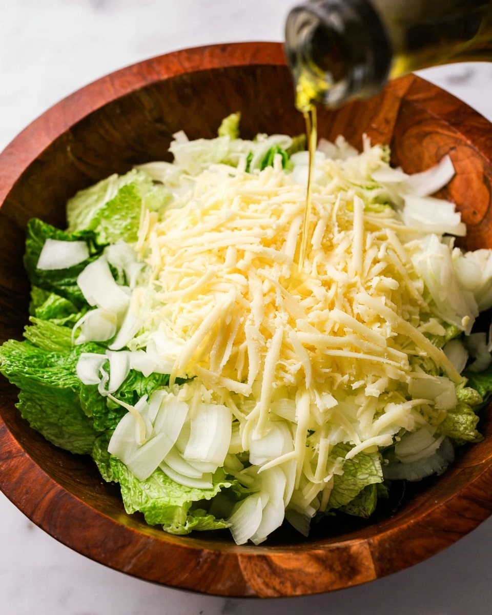A wooden bowl filled with fresh green lettuce leaves forms the bottom layer, followed by a layer of thinly sliced white onions. On top of the onions is a generous pile of finely shredded pale yellow cheese. From above, golden olive oil is being poured over all the layers. The bowl is placed on a white marbled surface. photo taken with an iphone --ar 4:5 --v 7