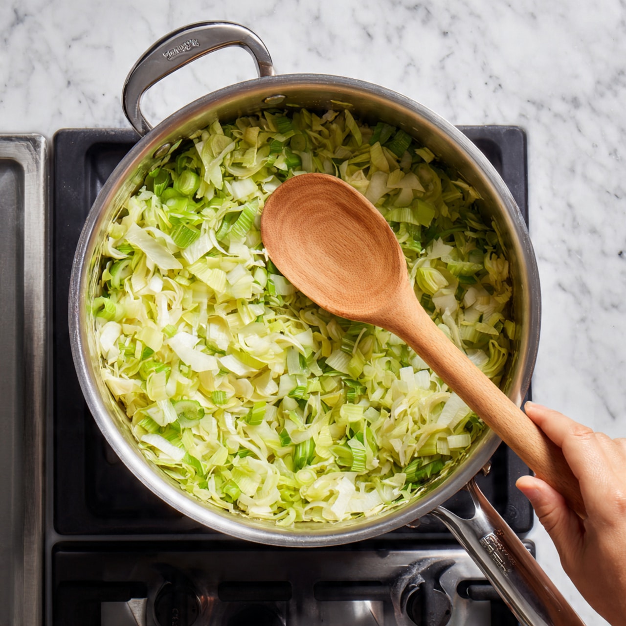A large silver cooking pot filled with chopped leeks in light green and white colors, arranged in an even layer inside. A wooden spoon with natural wood texture is sitting on top of the leeks inside the pot. The pot is placed on a black gas stove, but the surface visible around is changed to a white marbled texture. The woman's hand is holding the pot handle on the right side. photo taken with an iphone --ar 4:5 --v 7