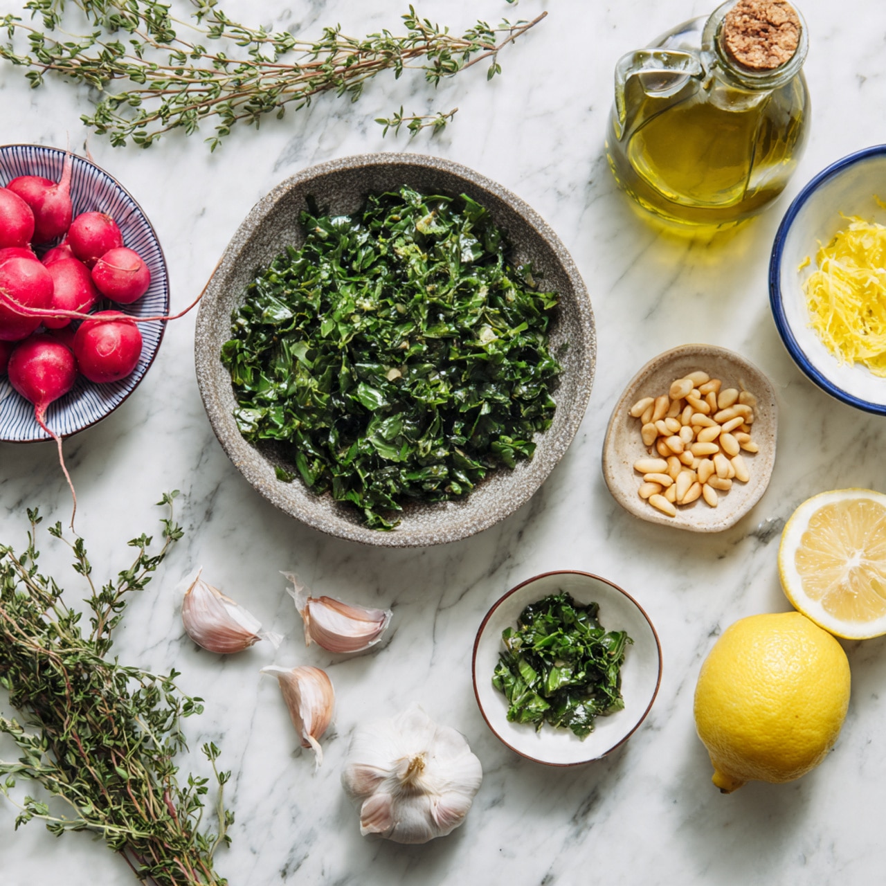 The image shows a white round plate with three small bowls on it, placed on a white marbled surface. The largest bowl is rough-textured and filled with chopped green leafy herbs. Next to it is a small white bowl holding some finely chopped green herbs. A small light brown-rimmed bowl contains shelled pine nuts. Around the plate, on the white marbled background, there are three garlic cloves near fresh thyme sprigs, two lemon halves with visible juicy pulp, a white bowl with a blue rim filled with bright red radishes, a small bowl with yellow lemon zest, and a clear greenish glass bottle of olive oil with a cork top. photo taken with an iphone --ar 4:5 --v 7