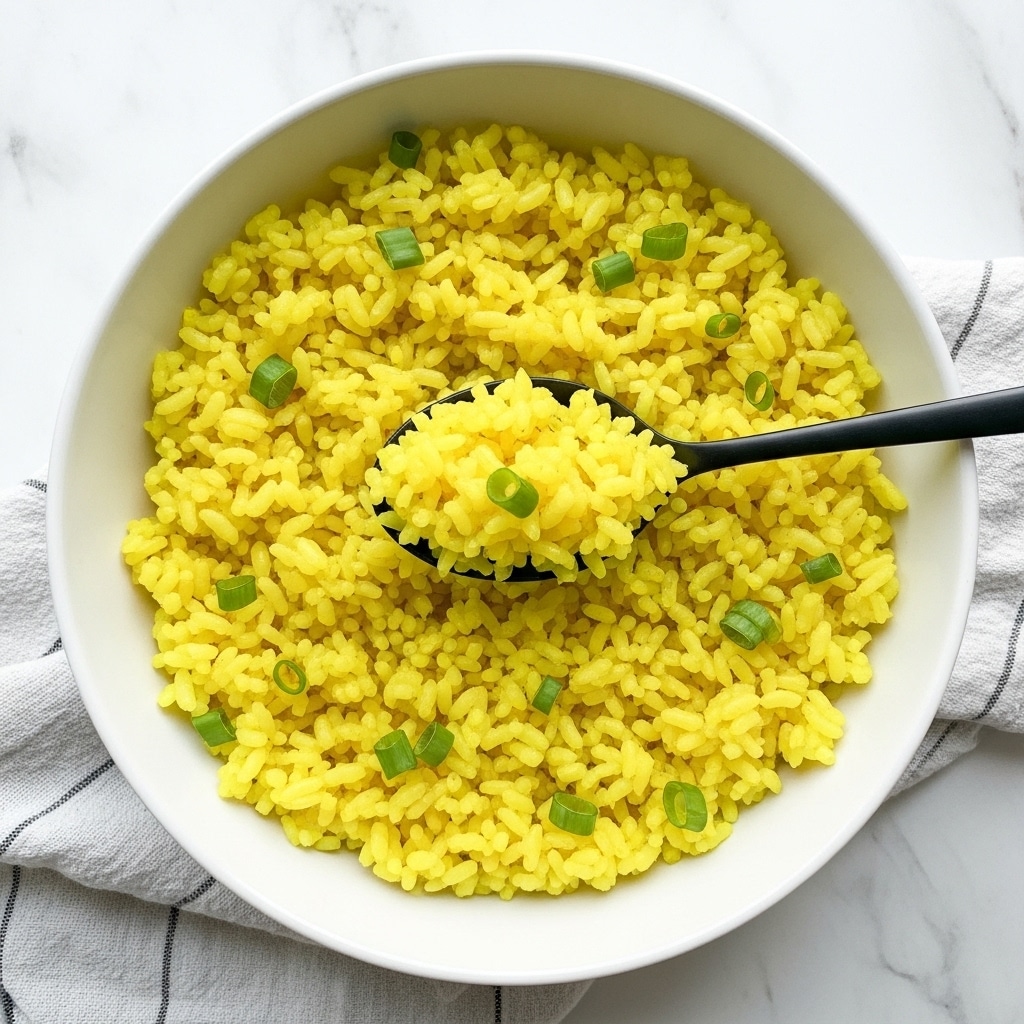 A close-up top view of a shiny silver pot filled with yellow rice, each grain distinct and slightly fluffy, with some grains showing lighter and darker yellow shades for texture. Inside the pot is a silver spoon partially buried in the rice, its handle resting on the right side. The pot sits on a white marbled surface, with the light reflecting softly on the metal and rice. photo taken with an iphone --ar 4:5 --v 7