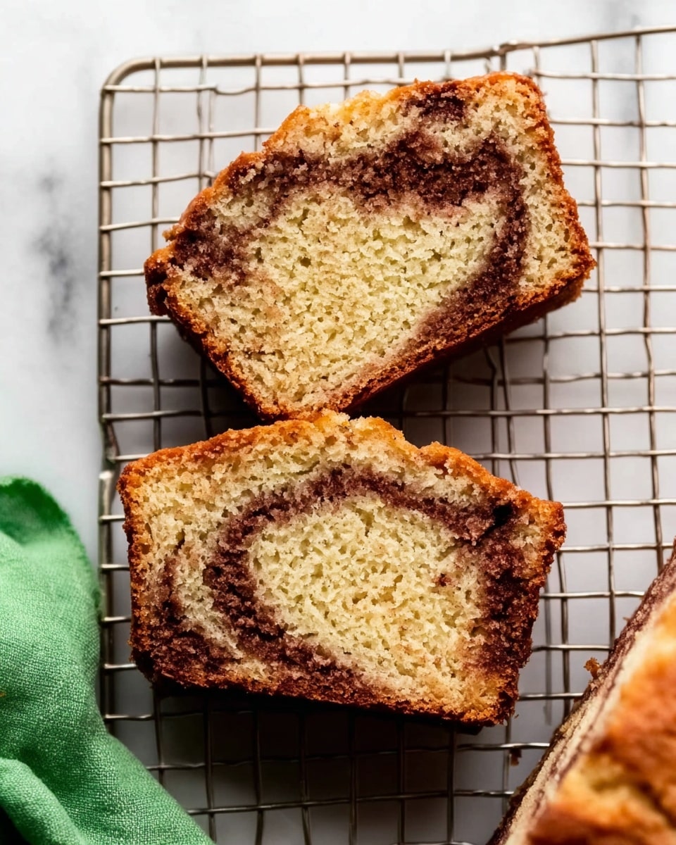 The image shows two slices of a loaf cake on a white marbled surface, placed on a metal cooling rack. Each slice reveals two layers inside: a dense, light brown cake layer with a soft texture and a dark brown cinnamon swirl running through the middle, creating a contrast. The cake's crust is golden brown and slightly crisp. One slice is fully visible in the center, while the edge of the other slice is partly shown at the top right. A green cloth is slightly visible in the lower-left corner of the image. The photo is taken with an iphone --ar 4:5 --v 7