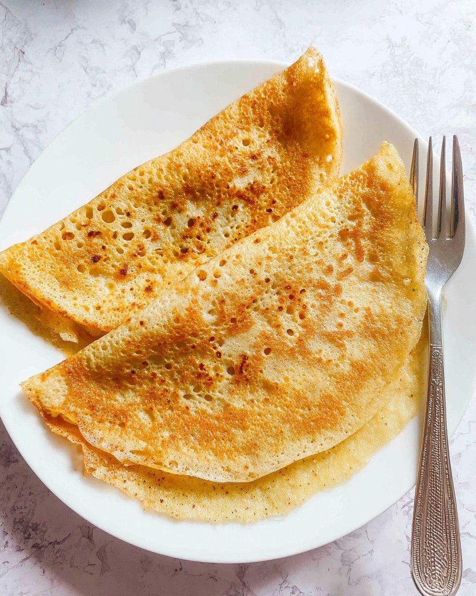 Two thin, folded crepes with a golden-brown color and a slightly crispy texture are placed on a white plate. Each crepe shows small holes and darker spots scattered across the surface, indicating a light toasty finish. The plate rests on a white marbled surface, and to the right of the plate, there is a silver fork with a textured handle. The overall look is warm and simple, highlighting the crepes’ airy and crisp layers photo taken with an iphone --ar 4:5 --v 7