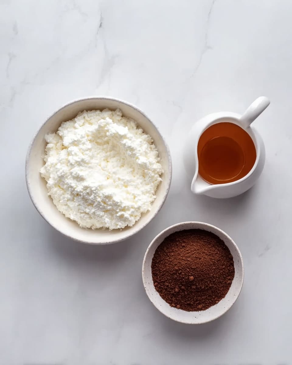 The image shows three white bowls placed on a white marbled surface. The largest bowl, positioned on the left, is filled with a white, soft, fluffy substance with a textured surface. To the right, there is a small white bowl filled with a dark brown, fine powder that looks smooth and even. Above this bowl, there is a small white jug filled with a clear amber-brown liquid. The arrangement is simple and neat, giving a clean and fresh look. Photo taken with an iphone --ar 4:5 --v 7