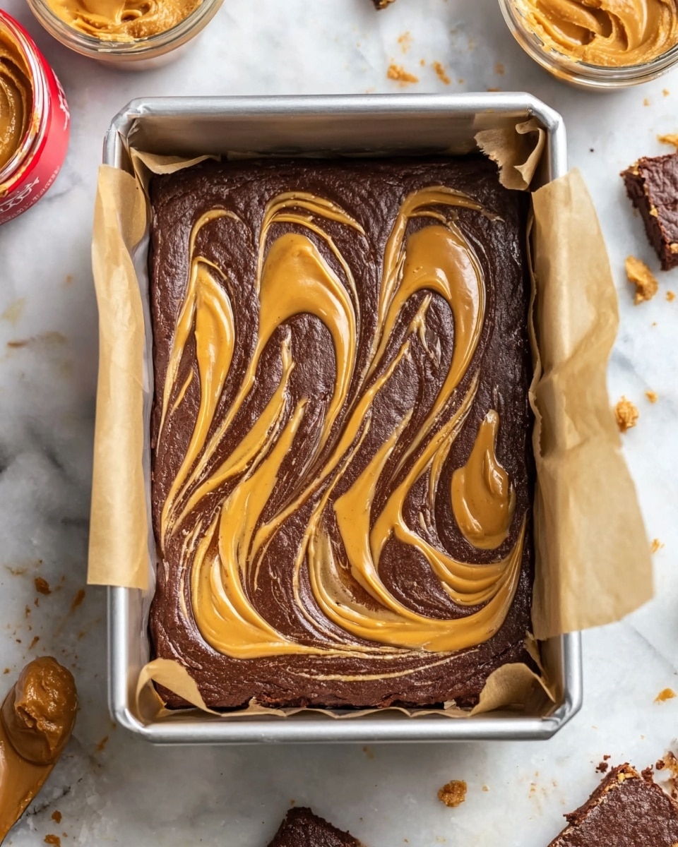The image shows a rectangular metal pan lined with parchment paper, filled with a dark brown chocolate batter. On top of the batter, there is a swirled pattern of a golden-brown peanut butter-like spread, creating four elongated loops evenly spaced from left to right. The peanut butter swirls have a smooth and creamy texture, contrasting with the thick, dense chocolate layer beneath. The pan is placed on a white marbled surface, surrounded by small crumbs and a few bowls with peanut butter. Photo taken with an iphone --ar 4:5 --v 7