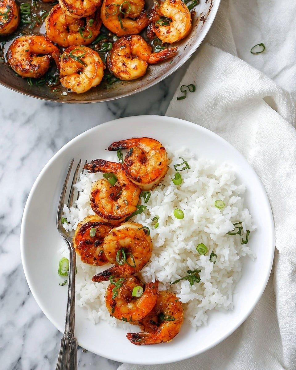 The image shows a white round plate on a white marbled surface with a serving of white rice spread on one side of the plate. Next to the rice are seven shrimp, cooked to a golden-orange color with a slight char, garnished with small green herbs and sliced green onions scattered on top. A silver fork rests on the edge of the plate, partially placed over the rice. In the top part of the image, there is a metal pan containing more cooked shrimp with the same golden color and green herb garnish. The background features a white cloth on the marbled surface. Photo taken with an iphone --ar 4:5 --v 7