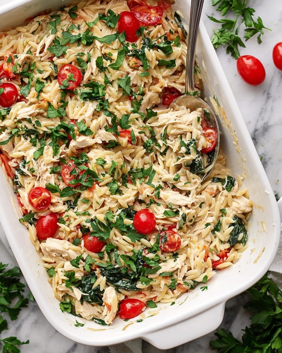 A white rectangular casserole dish filled with a creamy orzo pasta mixed with shredded light-colored chicken pieces, whole and halved bright red cherry tomatoes, and dark green spinach leaves. The dish is topped with a generous amount of fresh chopped parsley scattered over the top. A large silver spoon rests inside the dish, scooping up some of the mixture. The casserole dish is placed on a white marbled surface with some fresh parsley and cherry tomatoes nearby. Photo taken with an iphone --ar 4:5 --v 7