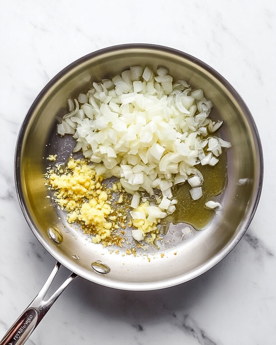 A stainless steel pan is shown from above, placed on a white marbled surface. Inside the pan, the largest layer is a pile of white chopped onions covering the upper half. Below the onions, there are two small piles of light yellow minced garlic and ginger, spaced apart on the pan's surface. A thin layer of shiny oil spreads under and around the ingredients, giving a slight glisten to the pan. The colors are mainly white and pale yellow against the silver of the pan. photo taken with an iphone --ar 4:5 --v 7