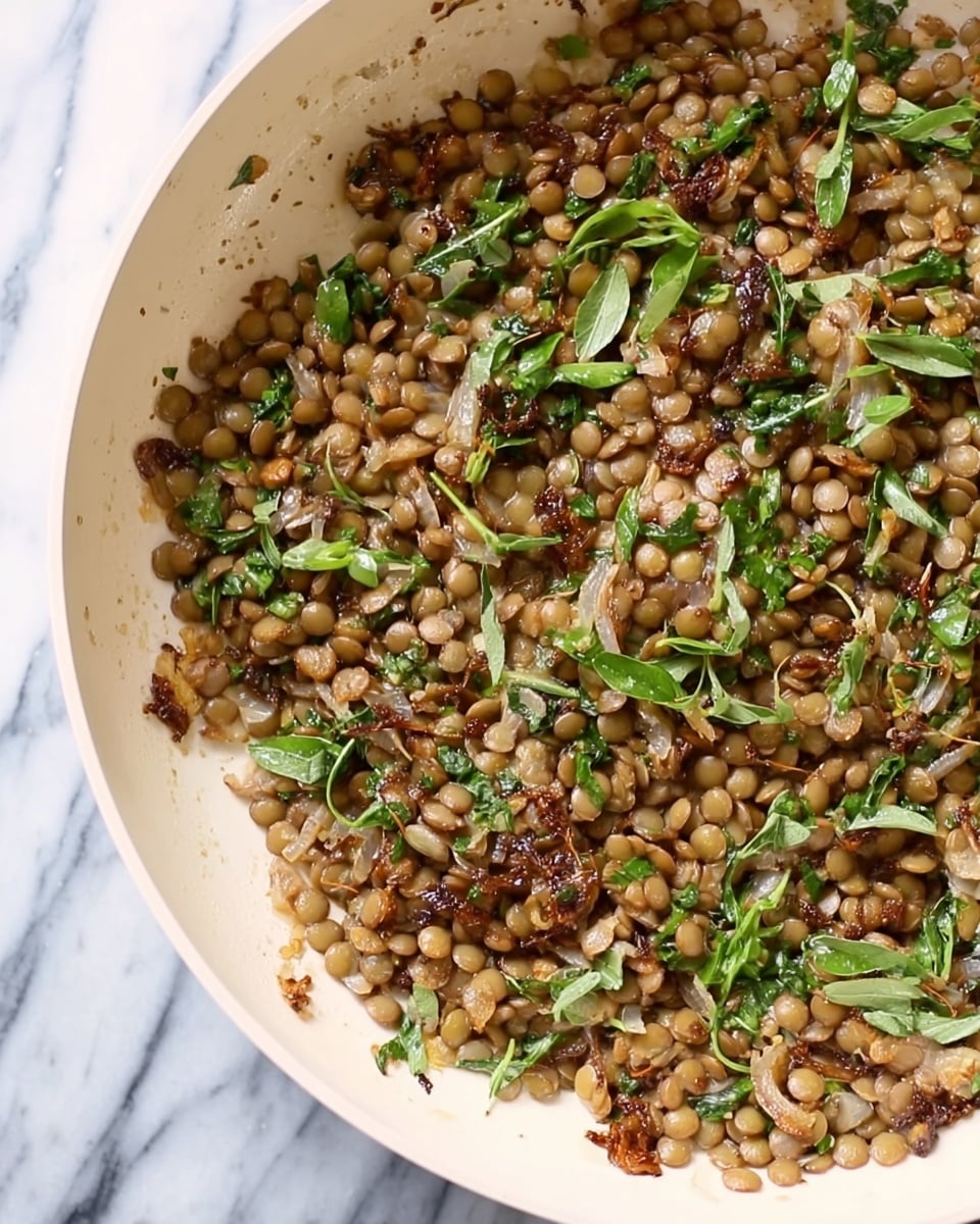 A white pan filled with cooked lentils mixed with small pieces of green herbs and bits of browned onions. The lentils are light brown and round, layered evenly across the pan, with some green herb leaves scattered throughout. The background is a white marbled texture. photo taken with an iphone --ar 4:5 --v 7