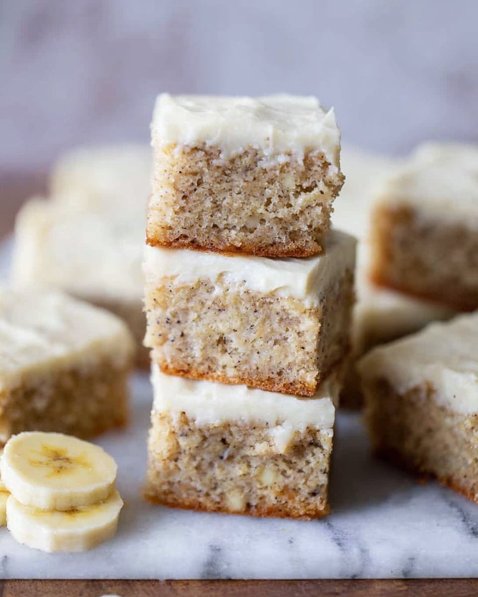 The image shows several square pieces of banana cake stacked on top of each other on a white marbled surface. Each cake piece has two layers: a moist, light brown cake base with small dark banana bits inside, and a thick, creamy white frosting layer on top with a smooth texture. The top piece is balanced between three bottom pieces, highlighting the soft texture of the cake. In the bottom left corner, there are a few slices of banana placed on the white marbled surface. The background is softly blurred, focusing attention on the cake pieces. photo taken with an iphone --ar 4:5 --v 7