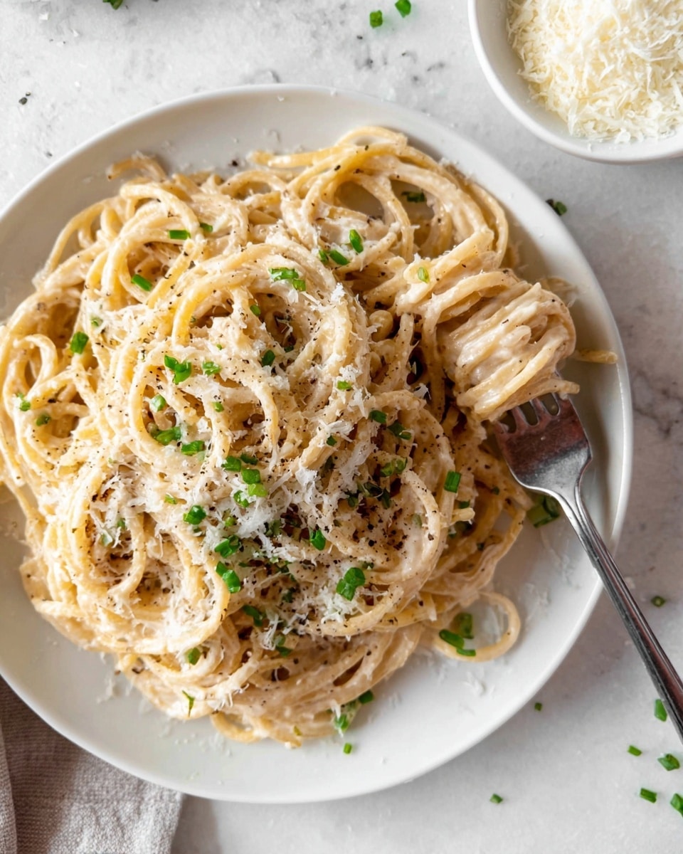 A white plate filled with a single layer of thick spaghetti noodles coated in a light creamy sauce, sprinkled with small bits of green chives and a generous amount of finely grated white cheese on top. A silver fork is twirling some noodles on the right side of the plate. The plate is set on a white marbled surface. Nearby, there is a small bowl with white grated cheese spilling slightly on the surface. Photo taken with an iphone --ar 4:5 --v 7