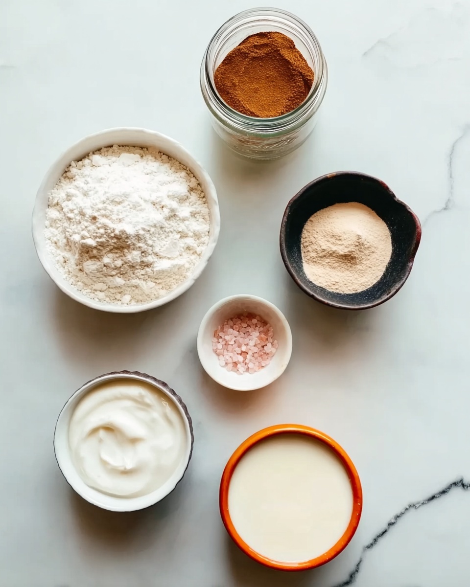 Greek Yogurt Donuts Recipe 5 The image shows six small containers placed on a white marbled surface. At the bottom left, there is a white bowl filled with white flour, showing a soft, powdery texture. Above it to the left is a glass jar with a metal lid holding a brown, fine spice, likely cinnamon. To the right of the jar is a small black bowl filled with a light tan powder. Further right, there is a small orange-rimmed white bowl containing pink salt grains. Below the salt and slightly left is a white bowl with smooth white yogurt or cream. Lastly, at the bottom right corner, a white bowl with an orange rim holds a creamy liquid. The containers are neatly arranged with some space between them. photo taken with an iphone --ar 4:5 --v 7