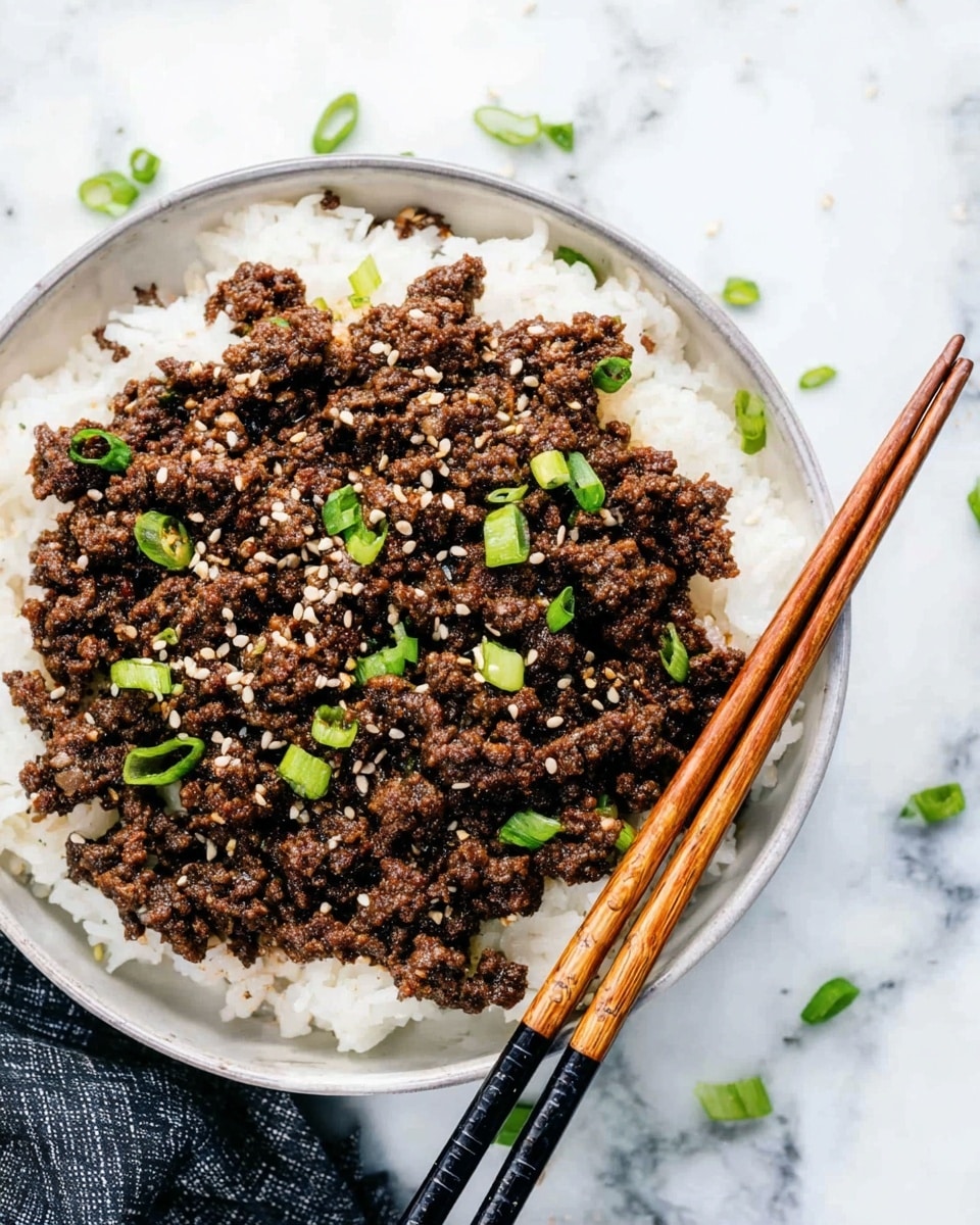 A white round bowl filled with a layer of white rice at the bottom, topped with a thick layer of cooked ground beef that is dark brown with a slightly crumbly texture. Scattered on the beef are small pieces of bright green chopped scallions and white sesame seeds. Two wooden chopsticks rest diagonally on the right side of the bowl, slightly touching the beef. The bowl is placed on a white marbled surface with some pieces of chopped scallions around it. Photo taken with an iphone --ar 4:5 --v 7