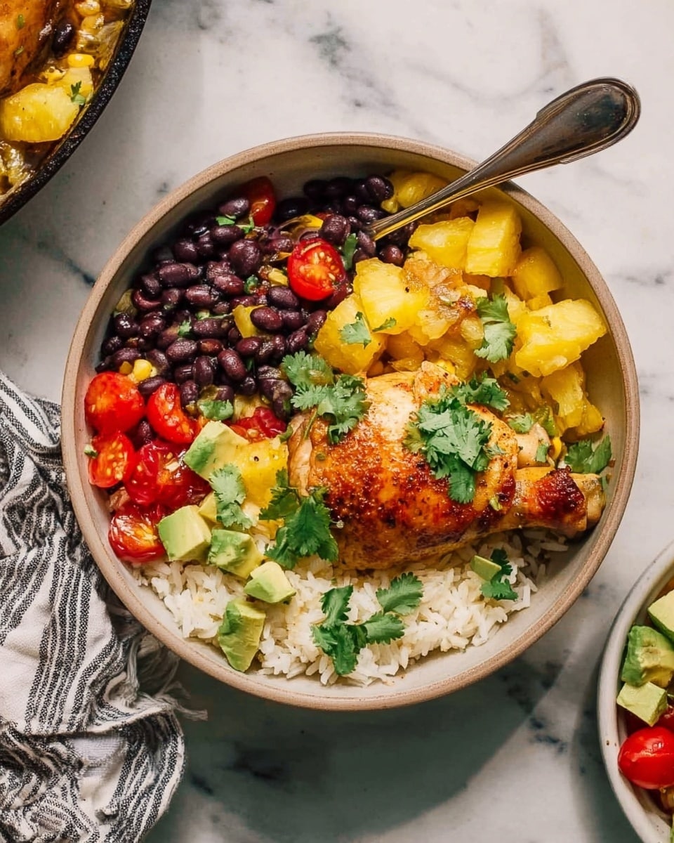 The image shows a bowl filled with a colorful layered meal on a white marbled surface. The bottom layer consists of fluffy white rice. On the right side of the bowl, there is a golden-brown cooked chicken leg with a slightly crispy skin, topped with fresh green cilantro leaves. Surrounding the chicken and rice are chunks of yellow pineapples and light yellow pieces of cooked onions with some roasted spots. On the left side, there is a small pile of black beans mixed with bright red cherry tomato halves. Scattered on top are small green avocado cubes adding a creamy texture and a vibrant contrast of color. A silver spoon rests inside the bowl, and a striped cloth is partially visible in the upper left corner. photo taken with an iphone --ar 4:5 --v 7