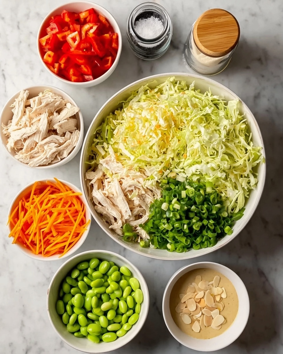 The image shows seven white bowls arranged on a white marbled surface. The largest bowl in the center is filled with two types of shredded greens; one side is light yellow cabbage, and the other side is green lettuce. Surrounding the large bowl are six smaller white bowls. At the top right, there is shredded white chicken. To its left, a bowl has bright red chopped bell peppers. Next to it, finely chopped green onions sit beside shredded orange carrots. At the bottom left, a bowl is filled with green edamame beans. In the middle bottom, there is a creamy sesame dressing in a small bowl. To the right, the last bowl has sliced almonds. A small jar of salt with a wooden top is also visible near the top left. The surface and background are white marble, and the image looks clear and bright. Photo taken with an iphone --ar 4:5 --v 7