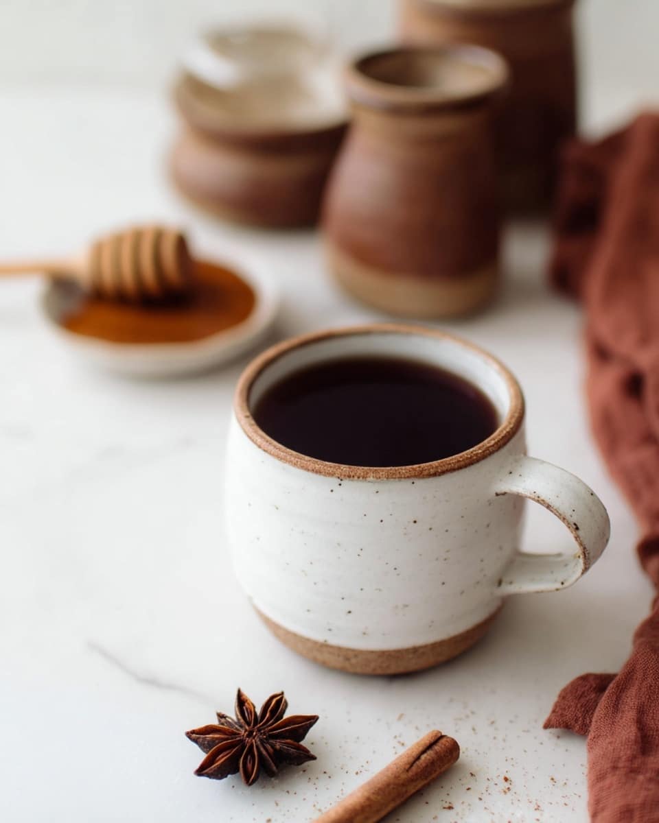 A white ceramic mug with a brown rim and small dark spots is filled with dark tea, placed on a white marbled surface. Near the mug, there is a star anise and a piece of cinnamon stick, both adding warm brown tones and natural textures. In the background, slightly blurred, are brown ceramic containers holding honey with a honey dipper resting on one and cinnamon powder in the other, all set against the white marbled backdrop. A rust-colored cloth is partially visible on the side, adding a soft and warm element to the scene. photo taken with an iphone --ar 4:5 --v 7