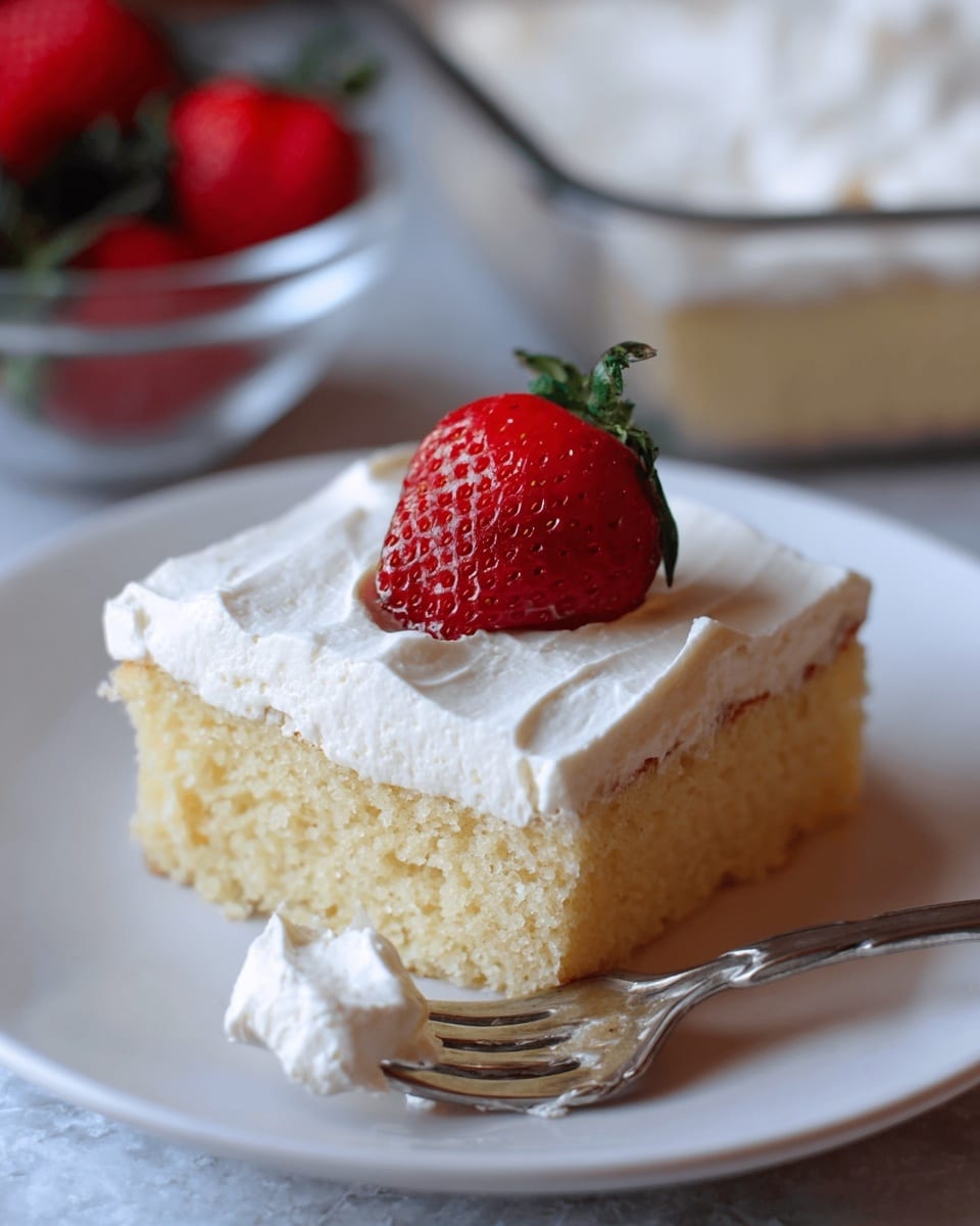 A square piece of light yellow sponge cake with one thick layer of smooth white frosting on top sits on a white plate with a white marbled texture surface in the background. A bright red strawberry with green leaves is placed in the middle on top of the frosting. A silver fork with some white frosting on the tines is positioned at the front right side of the plate. The cake shows soft texture with some small air holes inside. In the blurred background, there is a clear bowl with white cream and another bowl with red strawberries. Photo taken with an iphone --ar 4:5 --v 7