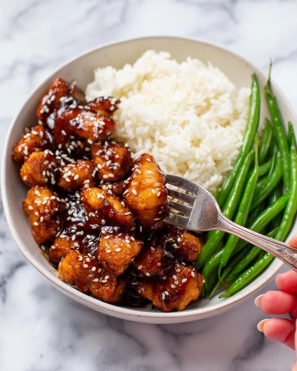 A white bowl holds a meal with three main parts: on the left side, there is a thick layer of golden-brown chicken pieces coated in a shiny dark sauce with white sesame seeds sprinkled on top; in the back right side, there is a fluffy layer of white rice with a soft texture; on the front right side, there is a smaller part of bright green whole green beans with a smooth surface. A silver fork pierces one piece of chicken in the center, with a woman's hand slightly holding it. The bowl sits on a white marbled surface. Photo taken with an iphone --ar 4:5 --v 7
