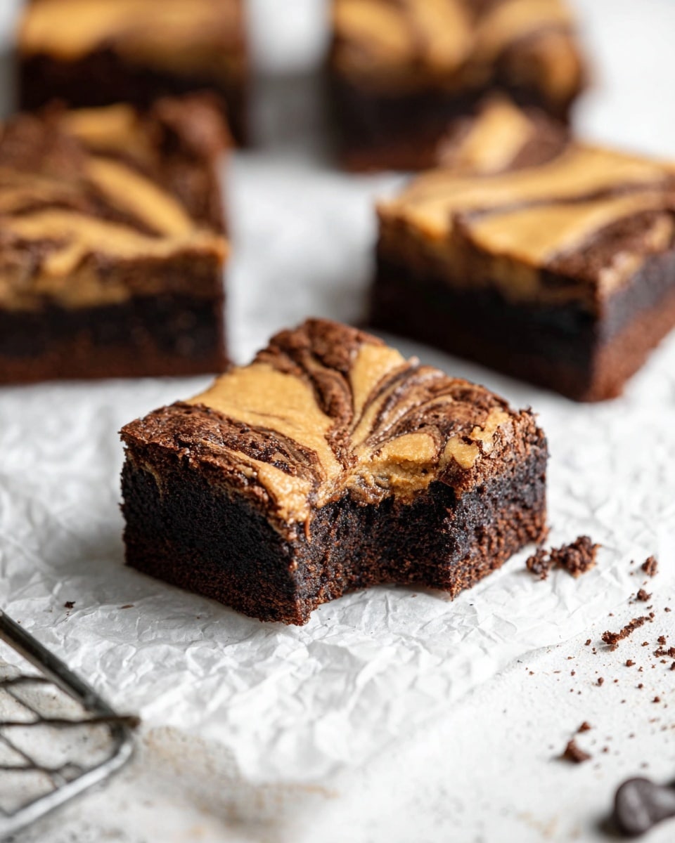 The image shows square brownies with two clear layers: a dense, dark brown bottom layer and a lighter, swirled caramel or peanut butter top layer with smooth swirls and curves. One brownie in the front has a bite taken out, showing the thick and moist dark chocolate inside. The brownies are placed on crumpled white baking paper over a white marbled surface with a few chocolate crumbs scattered around. The background is softly blurred, focusing on the front brownie, giving a warm and inviting look. photo taken with an iphone --ar 4:5 --v 7