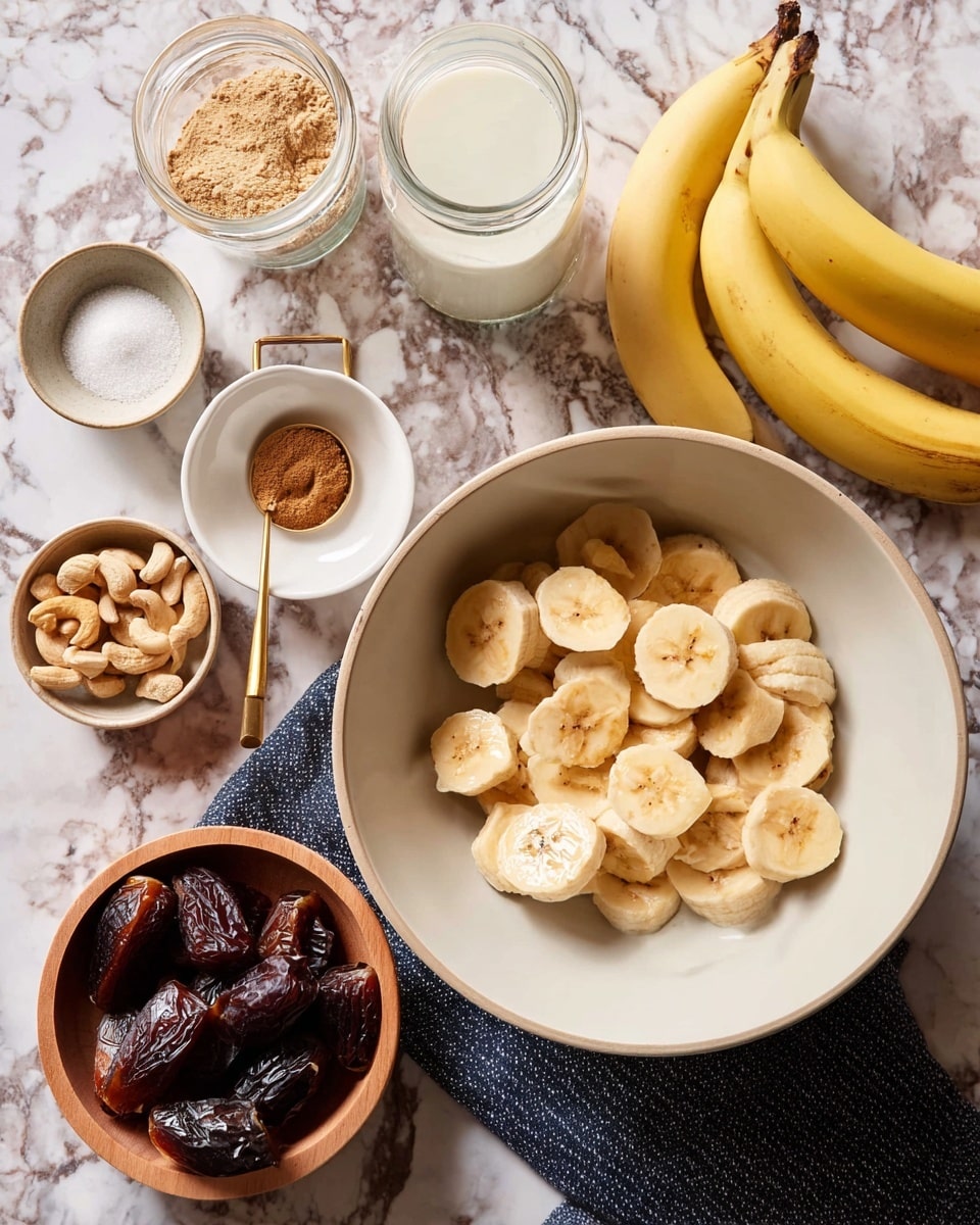 A white bowl filled with one layer of peeled and sliced bananas, light yellow with pale brown spots, is placed on a white marbled surface. To the right of the bowl, there are three whole yellow bananas with a curved shape. Surrounding the bowl, there is a small white bowl with a brown powder and a gold spoon inside, a small white bowl with white salt and some brown powder on top, a glass jar with white milk, a round tan wooden bowl filled with raw cashews, and a small beige bowl containing six dark brown dried dates. photo taken with an iphone --ar 4:5 --v 7