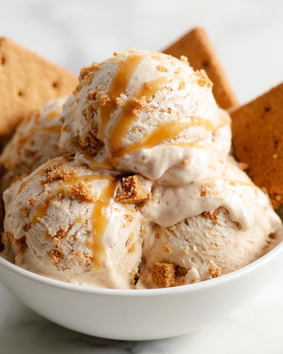 A close-up of three scoops of light beige ice cream with visible small chunks of graham crackers mixed inside, arranged tightly together in a white bowl. The ice cream has a creamy, smooth texture with some rough bits from the crackers. Golden caramel sauce is drizzled across the top scoop, dripping slightly down the sides. In the background, pieces of whole graham crackers peek out, adding contrast to the soft texture of the ice cream. The bowl sits on a white marbled surface, making the soft, warm tones of the ice cream and crackers stand out. Photo taken with an iphone --ar 4:5 --v 7