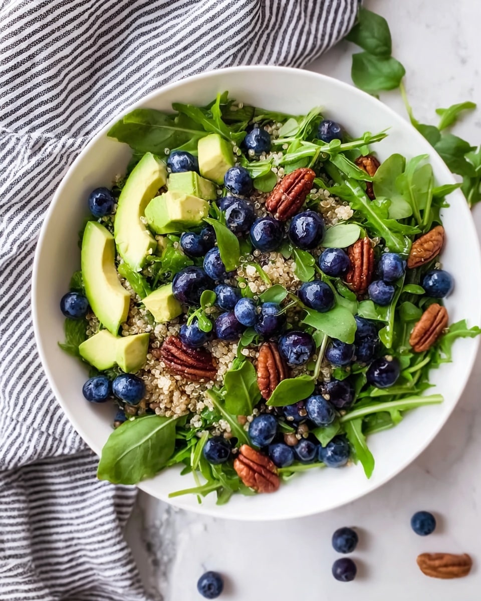 A white bowl filled with a fresh salad sits on a white marbled surface next to a black and white striped cloth. The salad has a base layer of green arugula leaves spread all around. On top, there are several blueberries scattered evenly, showing off their deep blue color and smooth texture. Mixed among them are light green avocado chunks cut into small cubes. There are also whole pecans placed in between the fruits and leaves, adding a brown textured layer. Small pieces of cooked quinoa are sprinkled evenly, adding a light beige grainy texture across the salad. Bright green basil leaves and microgreens sit on top for a fresh finish. Photo taken with an iphone --ar 4:5 --v 7